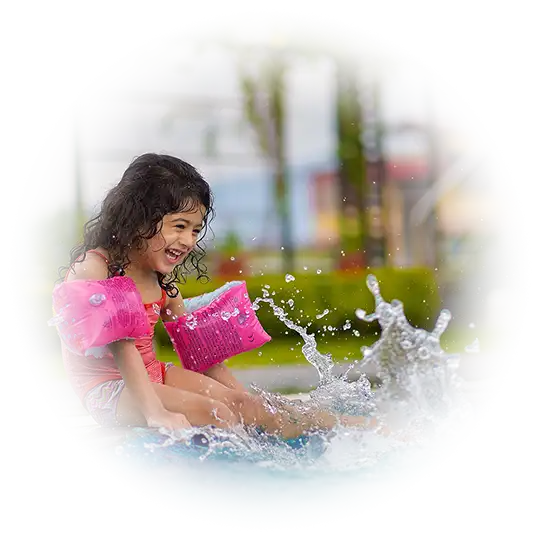 Petite fille avec des brassards roses assise au bord d'une piscine et éclaboussant l'eau avec ses pieds
